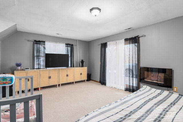 carpeted bedroom featuring a glass covered fireplace, baseboards, and visible vents