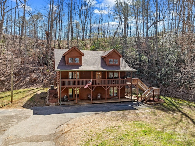 chalet / cabin with stairway, a wooded view, a shingled roof, a front lawn, and a deck