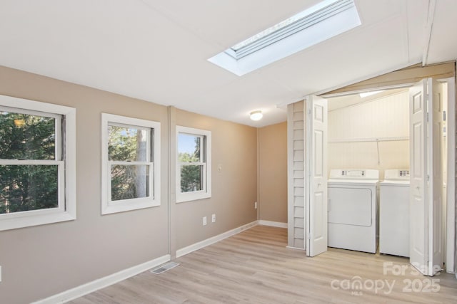 laundry room with light hardwood / wood-style floors, a skylight, and washing machine and clothes dryer