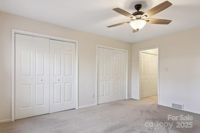 unfurnished bedroom featuring light carpet, ceiling fan, and multiple closets