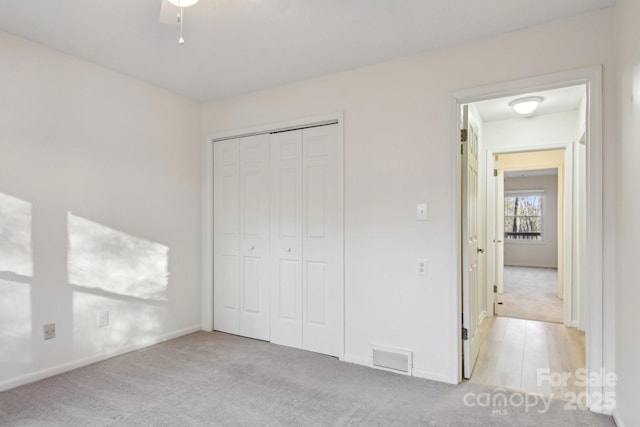 unfurnished bedroom featuring ceiling fan, light colored carpet, and a closet