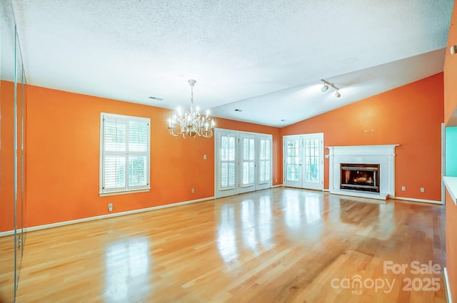 unfurnished living room featuring hardwood / wood-style floors, a textured ceiling, an inviting chandelier, and vaulted ceiling