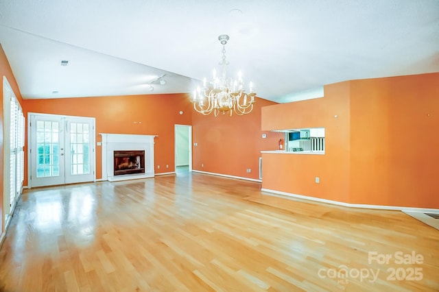 unfurnished living room featuring a notable chandelier, wood-type flooring, french doors, and vaulted ceiling