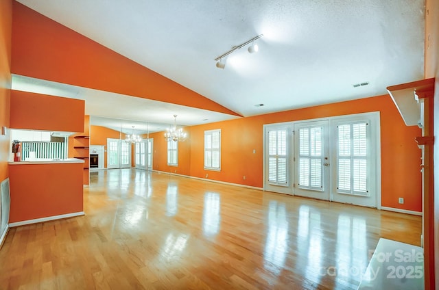 unfurnished living room with plenty of natural light, a chandelier, vaulted ceiling, and light wood-type flooring