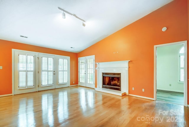 unfurnished living room featuring rail lighting, lofted ceiling, and light wood-type flooring