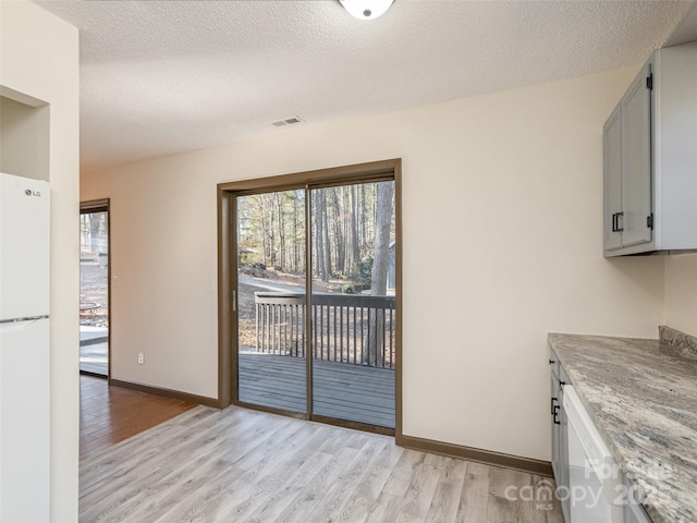 unfurnished dining area with a textured ceiling and light hardwood / wood-style flooring