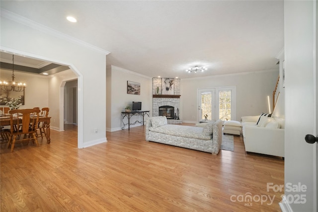 living area with arched walkways, a stone fireplace, light wood-type flooring, and baseboards