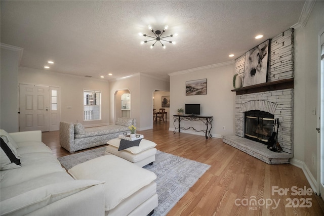 living area featuring arched walkways, light wood-style flooring, crown molding, a textured ceiling, and a fireplace