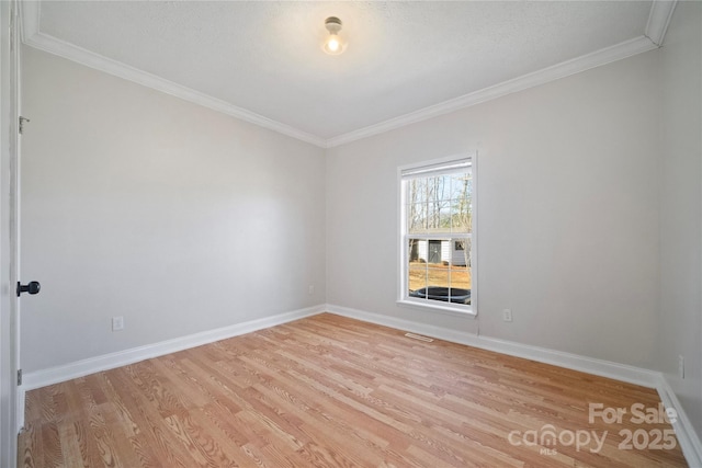 empty room featuring light wood-style floors, visible vents, baseboards, and ornamental molding