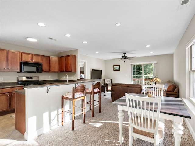 kitchen featuring a kitchen bar, ceiling fan, light colored carpet, and stainless steel range with gas stovetop