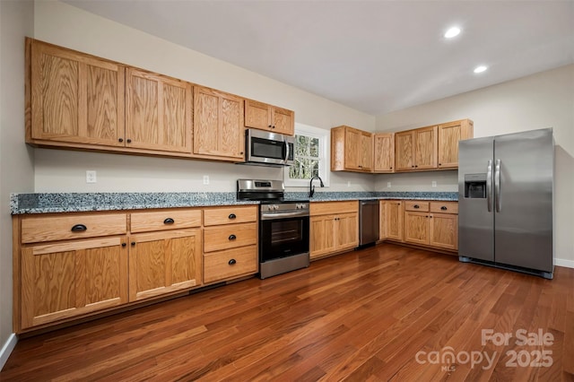 kitchen featuring appliances with stainless steel finishes, dark hardwood / wood-style floors, dark stone counters, and sink