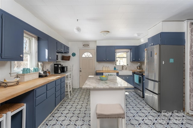 kitchen featuring blue cabinetry, appliances with stainless steel finishes, a kitchen bar, and sink