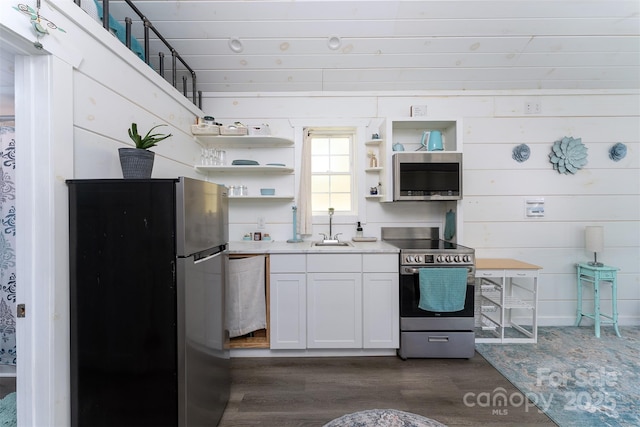 kitchen featuring sink, white cabinetry, stainless steel appliances, and wooden walls