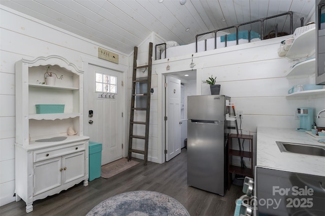 kitchen with wood walls, wooden ceiling, sink, white cabinetry, and stainless steel refrigerator