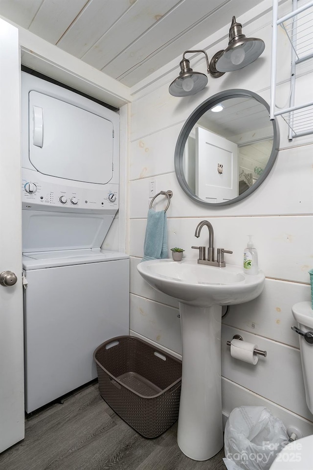 bathroom with wood-type flooring, stacked washing maching and dryer, and wooden walls