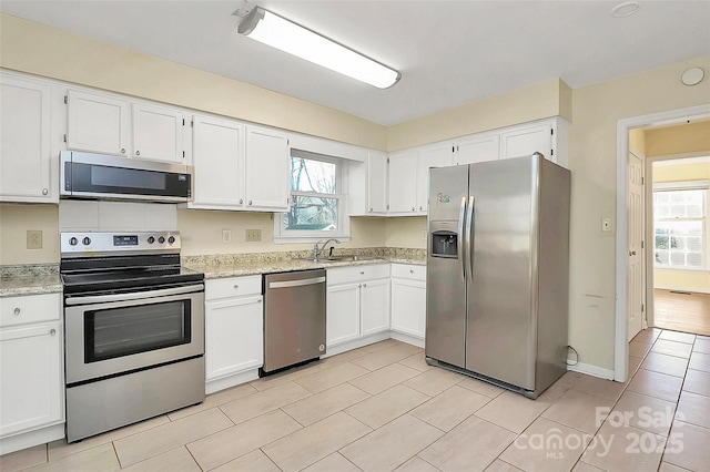 kitchen featuring light stone countertops, white cabinets, appliances with stainless steel finishes, sink, and light tile patterned flooring