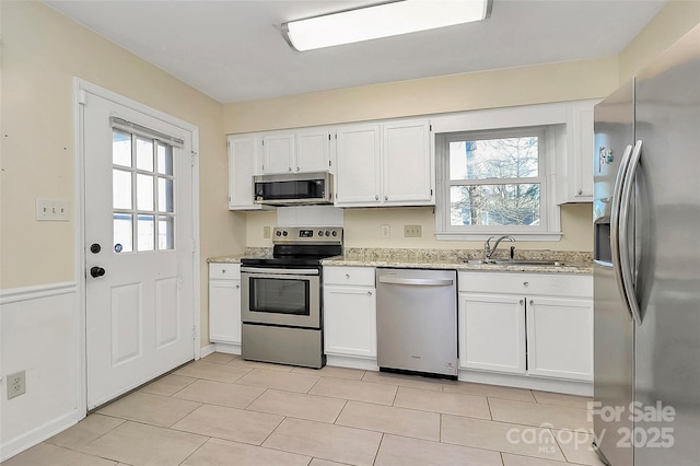 kitchen featuring appliances with stainless steel finishes, white cabinets, sink, light stone counters, and light tile patterned flooring