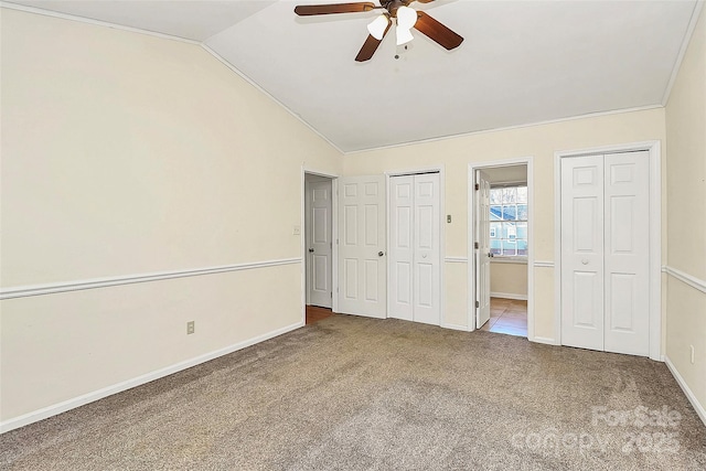 unfurnished bedroom featuring ceiling fan, two closets, carpet floors, and vaulted ceiling