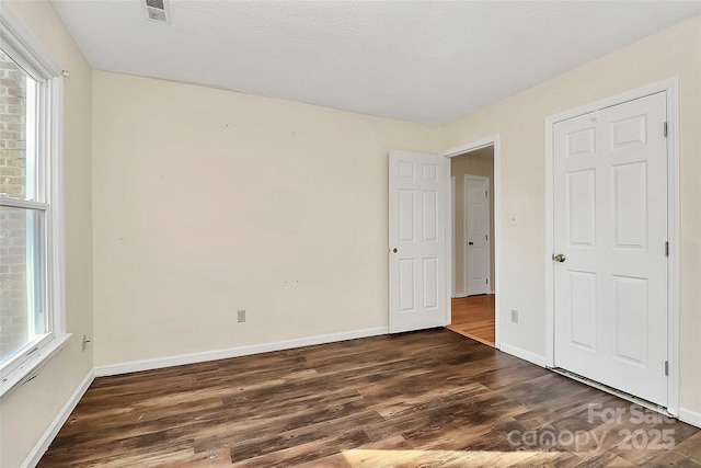 unfurnished bedroom with dark wood-type flooring, multiple windows, and a textured ceiling