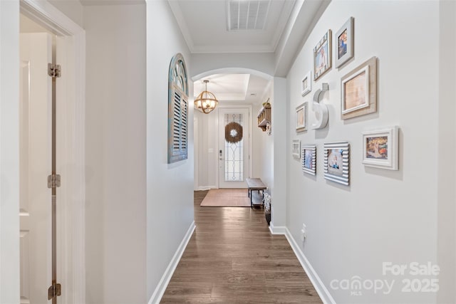 hall with a chandelier, ornamental molding, and dark wood-type flooring