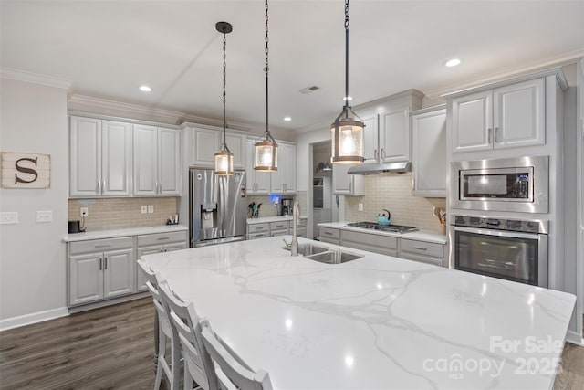 kitchen featuring light stone countertops, decorative light fixtures, stainless steel appliances, sink, and a kitchen island with sink