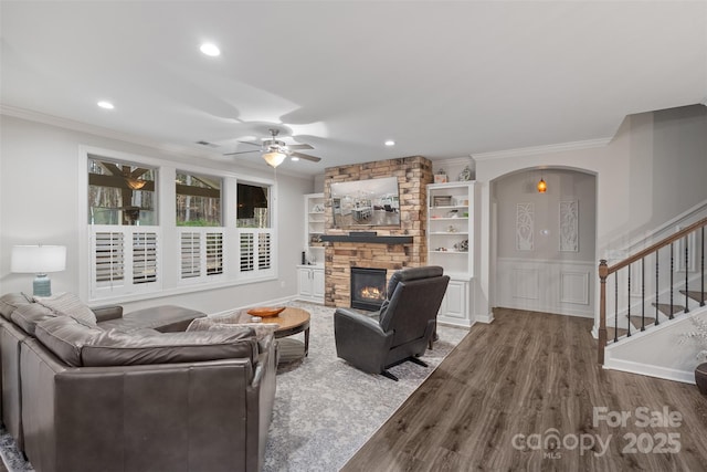 living room with hardwood / wood-style flooring, a stone fireplace, ceiling fan, and crown molding