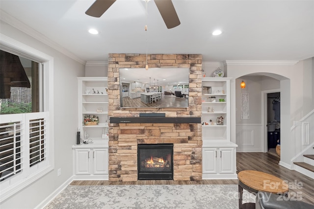 living room with crown molding, ceiling fan, built in shelves, hardwood / wood-style floors, and a fireplace