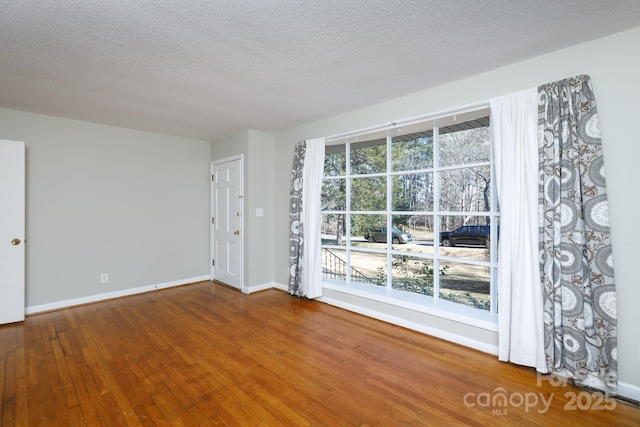 spare room featuring a textured ceiling, hardwood / wood-style flooring, and a healthy amount of sunlight