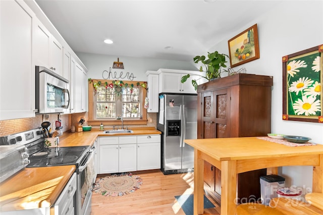 kitchen with white cabinets, stainless steel appliances, tasteful backsplash, sink, and light wood-type flooring