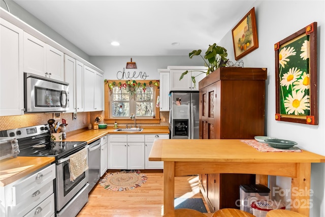 kitchen featuring stainless steel appliances, backsplash, white cabinets, light hardwood / wood-style flooring, and sink