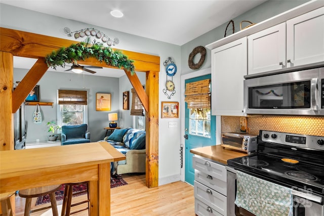 kitchen with white cabinetry, stainless steel appliances, decorative backsplash, light wood-type flooring, and ceiling fan