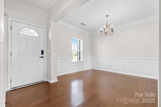 entrance foyer with dark hardwood / wood-style flooring, crown molding, and a notable chandelier