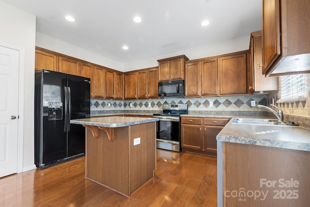 kitchen with dark hardwood / wood-style floors, a kitchen island, black appliances, sink, and a breakfast bar area