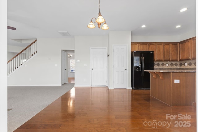 kitchen featuring decorative light fixtures, an inviting chandelier, black fridge with ice dispenser, a kitchen breakfast bar, and dark carpet