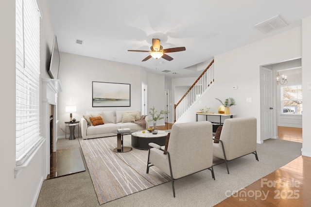 carpeted living room featuring a brick fireplace and ceiling fan with notable chandelier