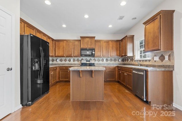 kitchen featuring black appliances, a center island, sink, hardwood / wood-style flooring, and light stone counters