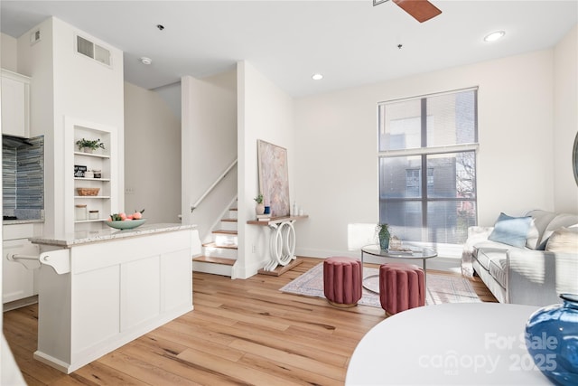 living room with ceiling fan, light hardwood / wood-style flooring, and built in shelves