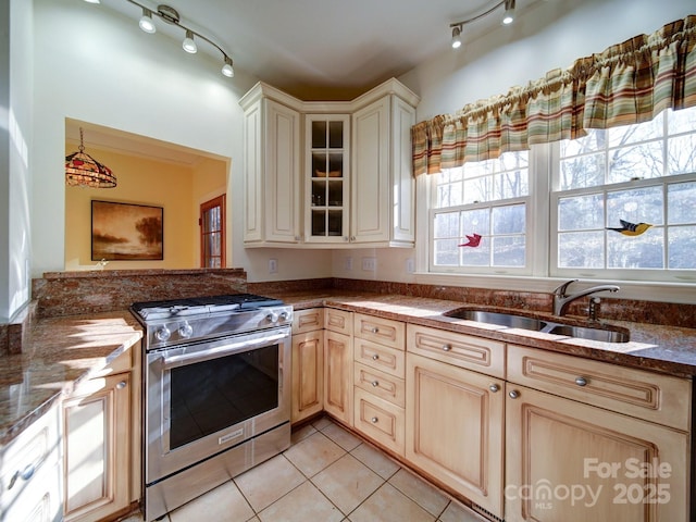 kitchen with light tile patterned flooring, stainless steel stove, dark stone counters, and sink