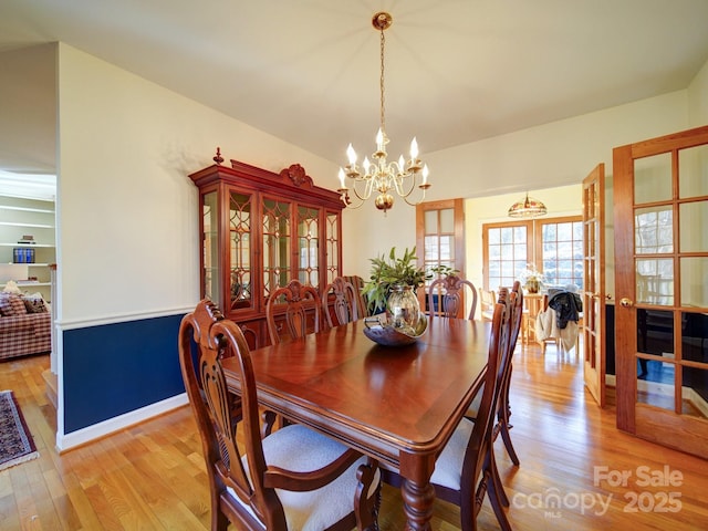 dining area with a chandelier, french doors, and light wood-type flooring