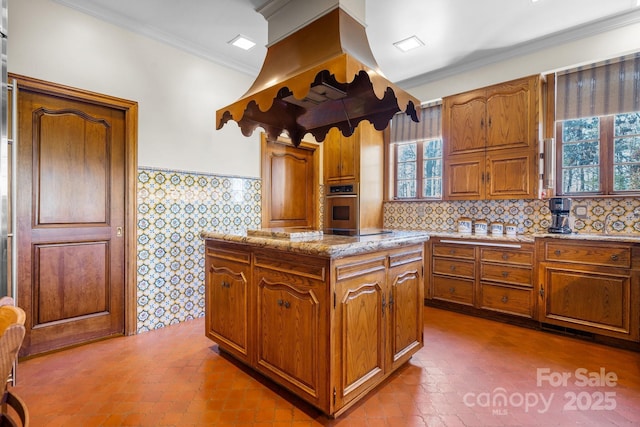 kitchen with island range hood, ornamental molding, stainless steel oven, black electric stovetop, and light stone countertops