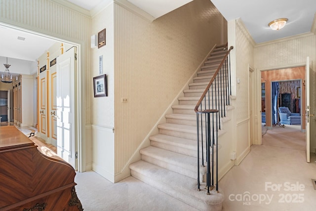 stairway with ornamental molding, carpet floors, and a notable chandelier