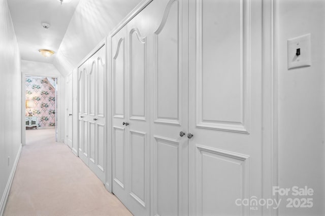 hall featuring lofted ceiling and light colored carpet