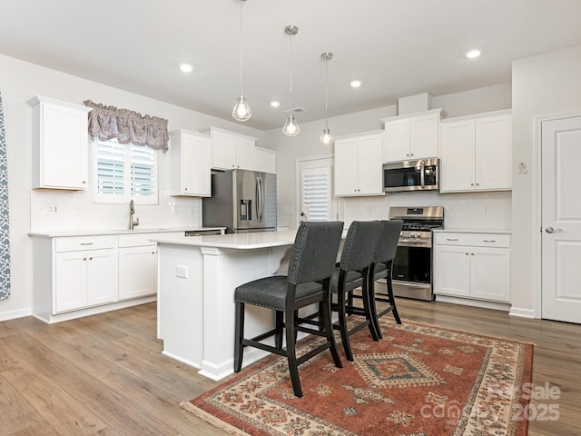 kitchen featuring decorative light fixtures, white cabinets, a kitchen bar, a kitchen island, and appliances with stainless steel finishes