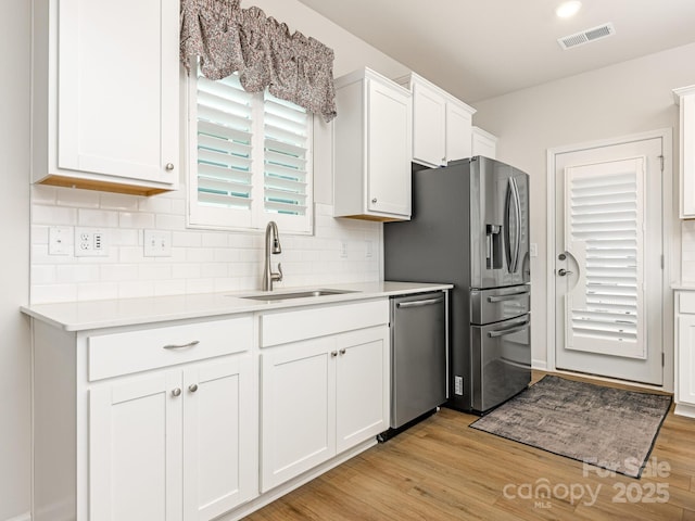 kitchen featuring light hardwood / wood-style floors, stainless steel appliances, white cabinets, backsplash, and sink