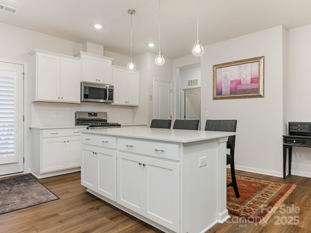 kitchen featuring appliances with stainless steel finishes, a center island, decorative backsplash, white cabinetry, and decorative light fixtures