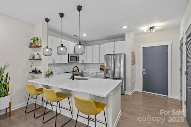 kitchen with appliances with stainless steel finishes, kitchen peninsula, sink, white cabinetry, and tasteful backsplash