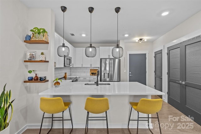 kitchen featuring white cabinets, kitchen peninsula, a breakfast bar area, backsplash, and appliances with stainless steel finishes