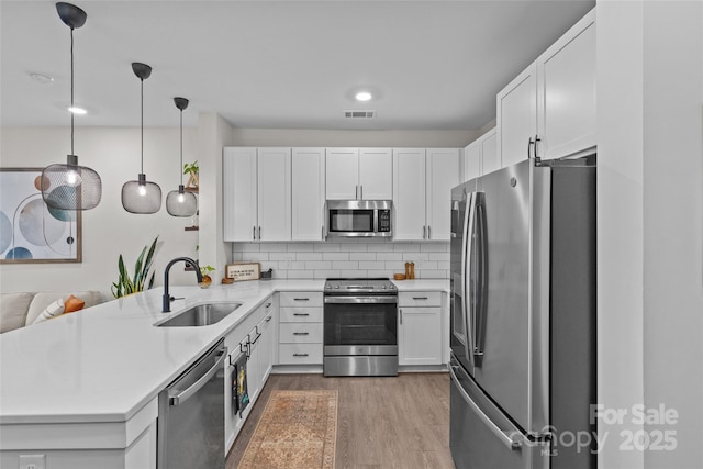 kitchen with kitchen peninsula, pendant lighting, white cabinets, appliances with stainless steel finishes, and sink