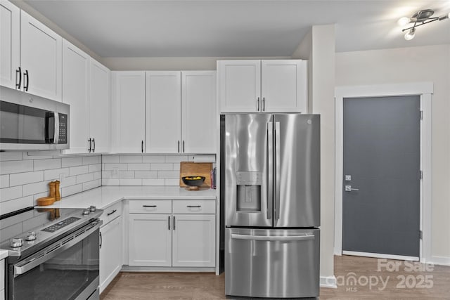 kitchen with white cabinets, appliances with stainless steel finishes, hardwood / wood-style flooring, and decorative backsplash