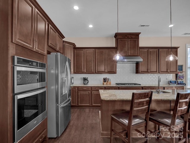 kitchen with a center island with sink, light stone countertops, stainless steel appliances, and pendant lighting